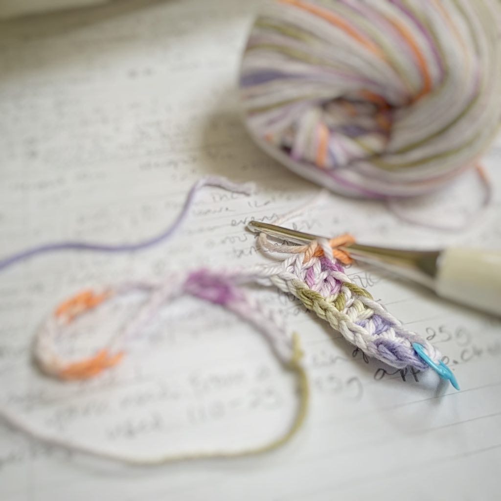 image of yarn, crochet hook on top of a notebook with beginnings of a crochet project visible